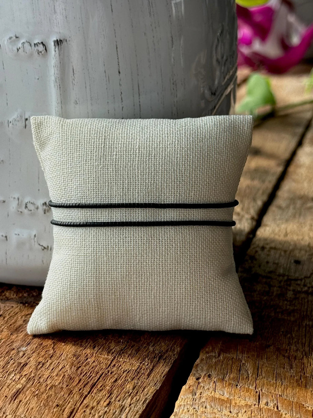 Handmade glass seed bead bracelet on black cord displayed on beige pillow, rustic wood background