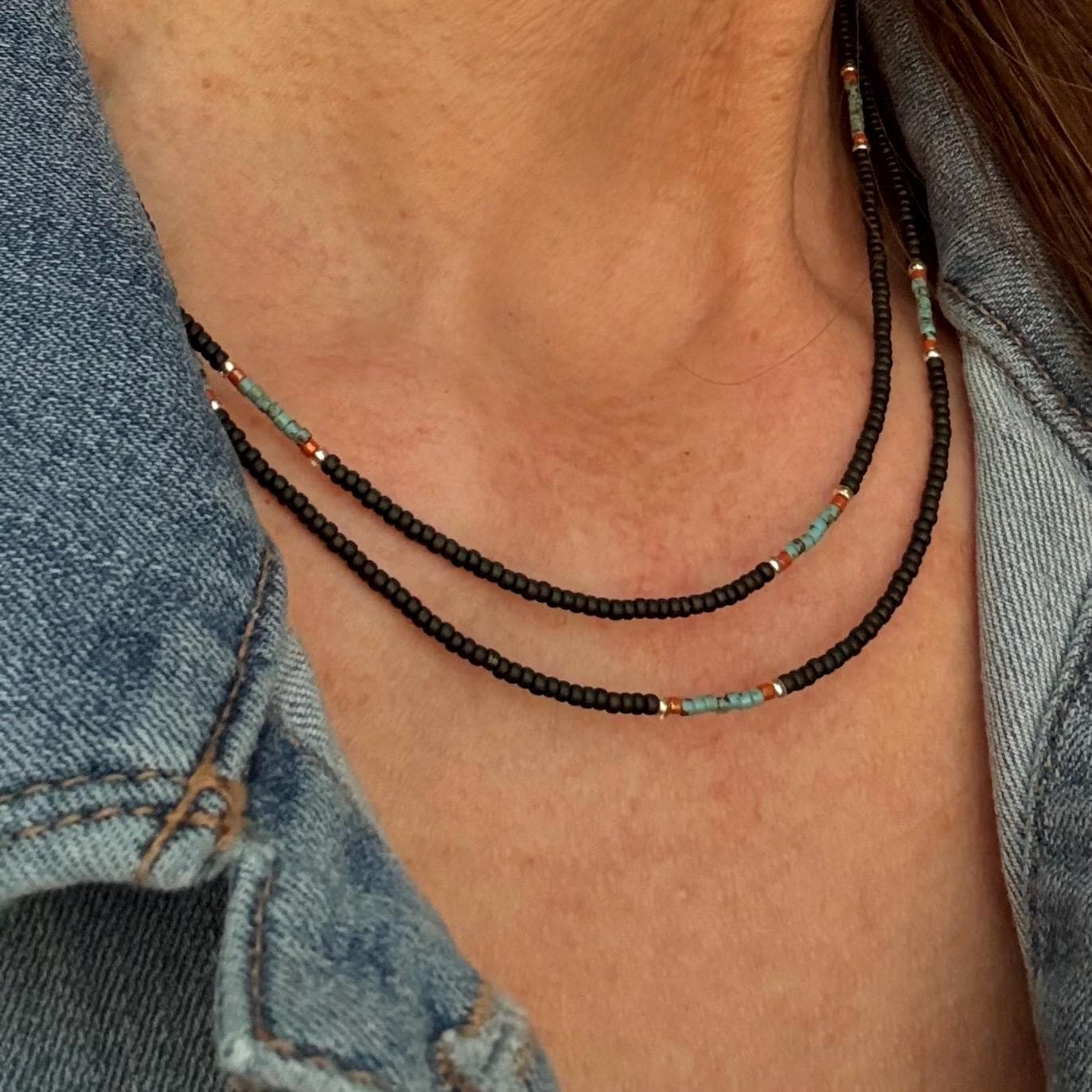 A brown, turquoise, coral and silver beaded wrap bracelet is worn as a necklace, double draped, around a woman's neck.