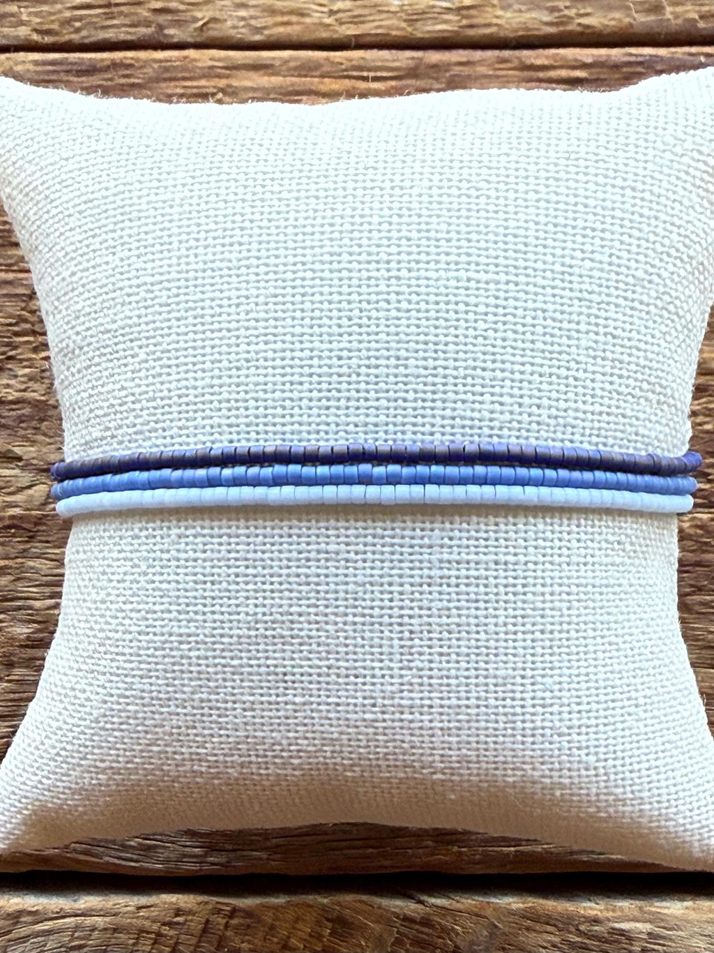 Handmade glass seed bead bracelets in blue tones on a woven pillow, rustic wood background