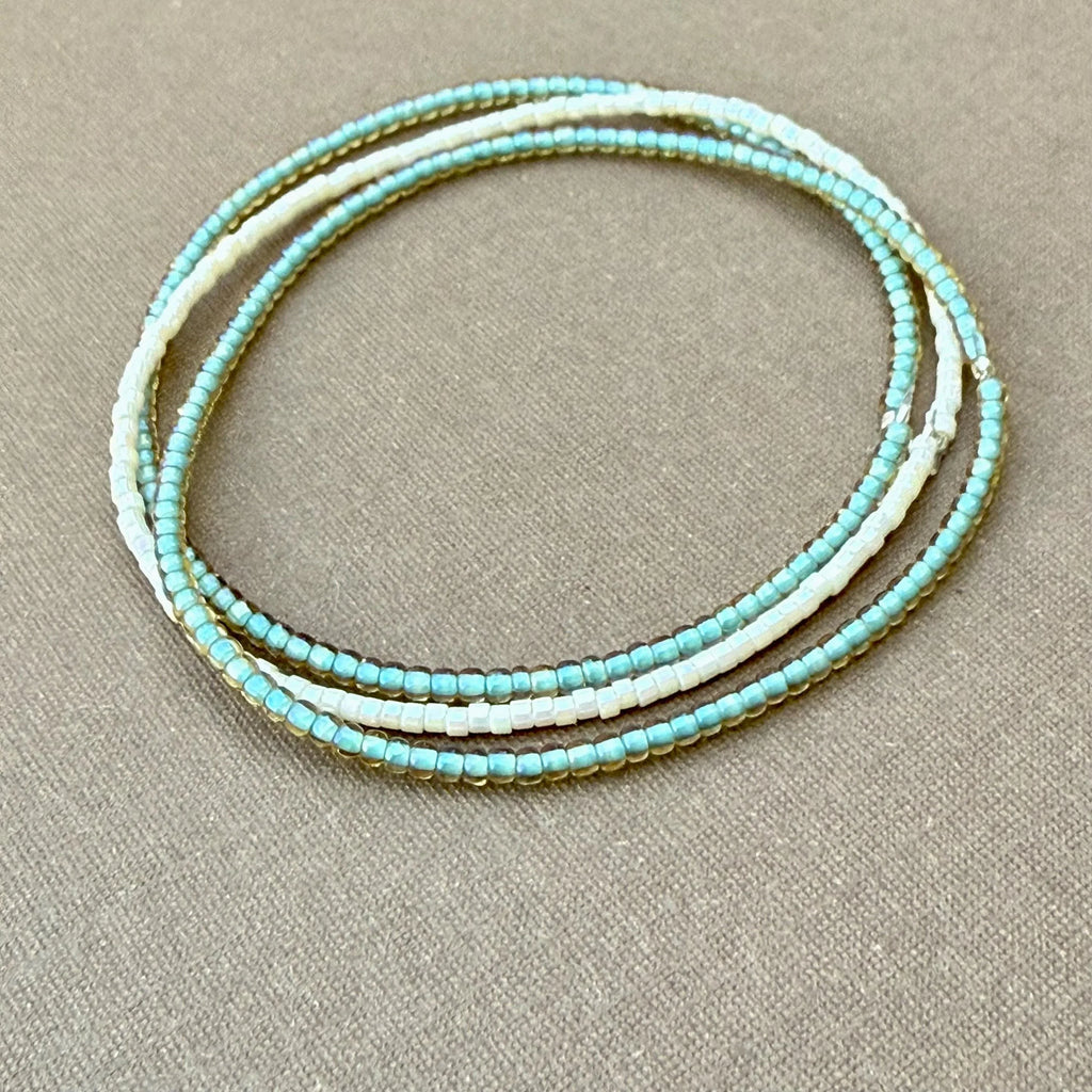 Handmade glass seed bead bracelet in shades of turquoise and white on beige fabric background