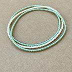 Handmade glass seed bead bracelet in shades of turquoise and white on beige fabric background