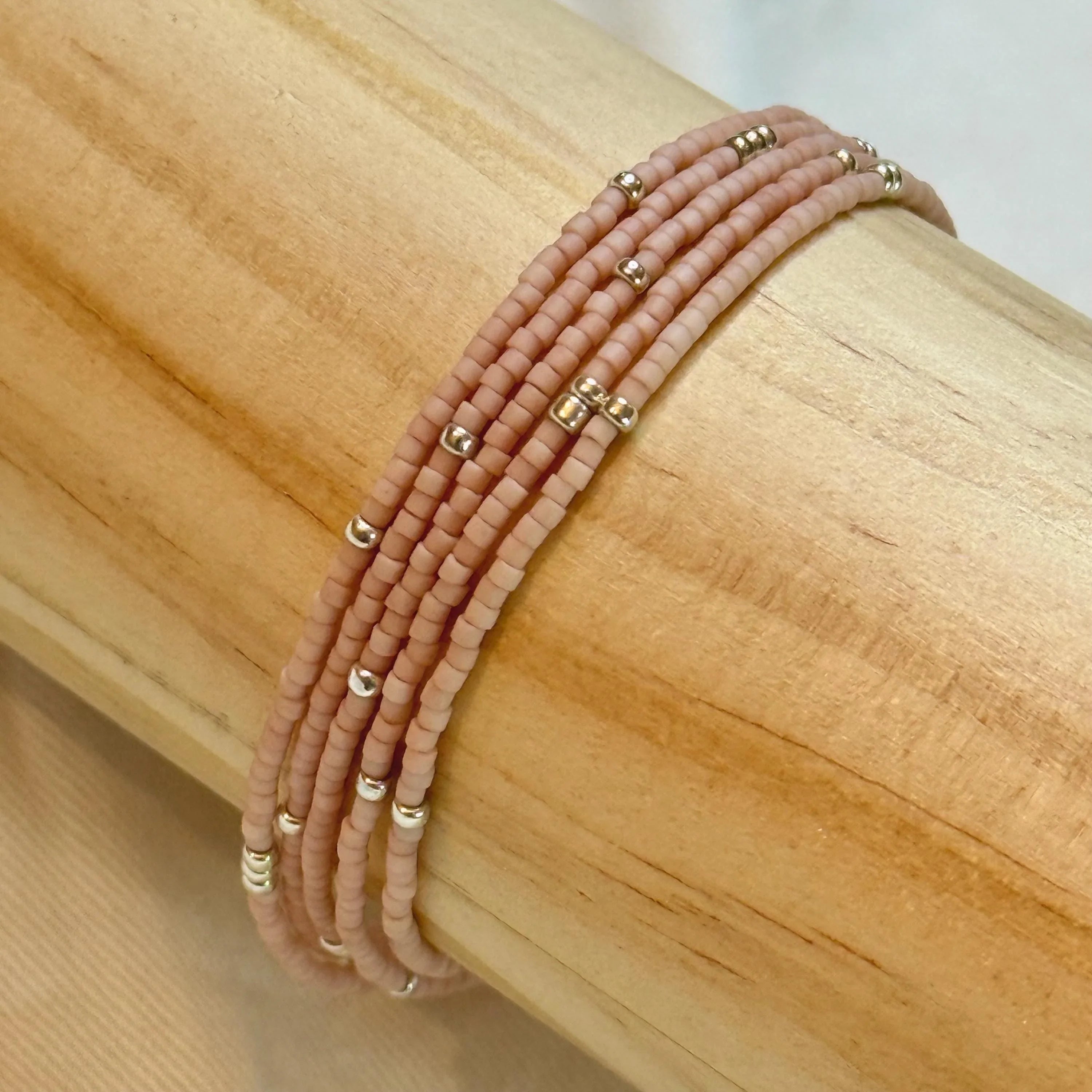 Handmade pink glass seed bead bracelet with gold accents on wood display