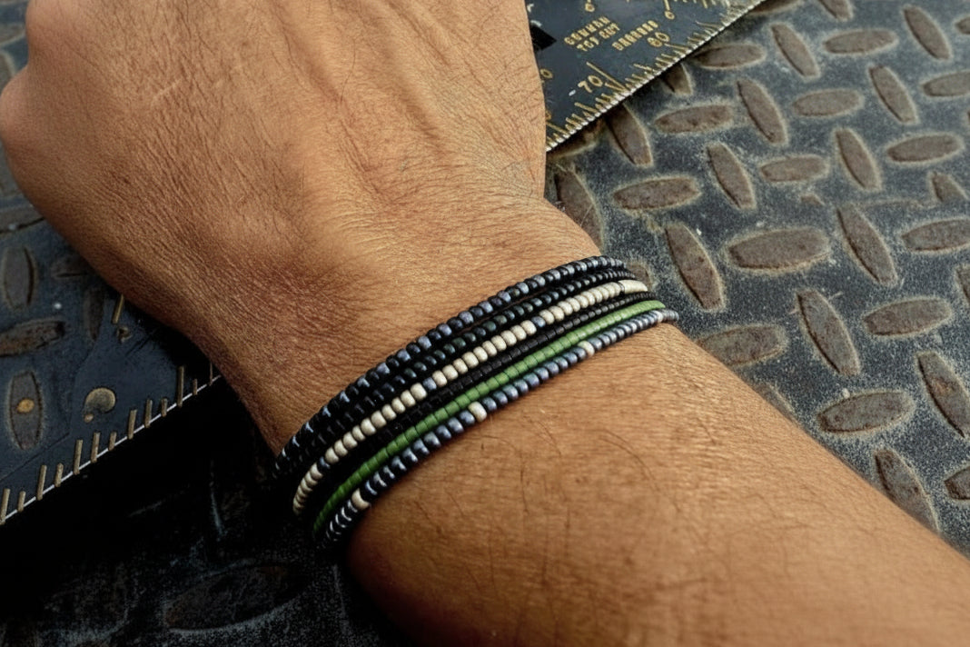 Hand wearing multi-stack glass seed bead bracelets in black, green, blue and silver tones