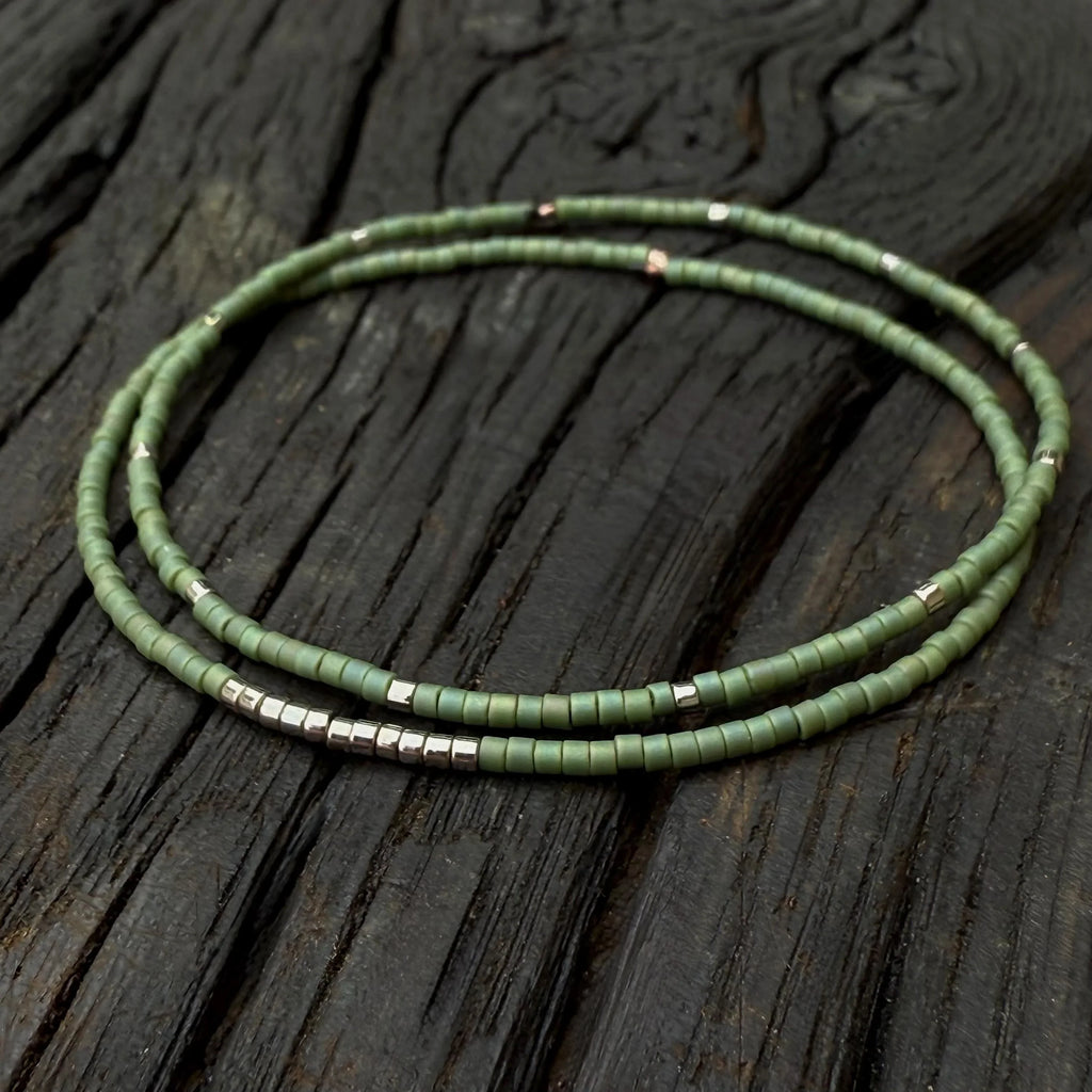 Handmade green glass seed bead bracelet with silver accents on rustic wood background