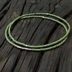 Handmade green glass seed bead bracelet with silver accents on rustic wood background