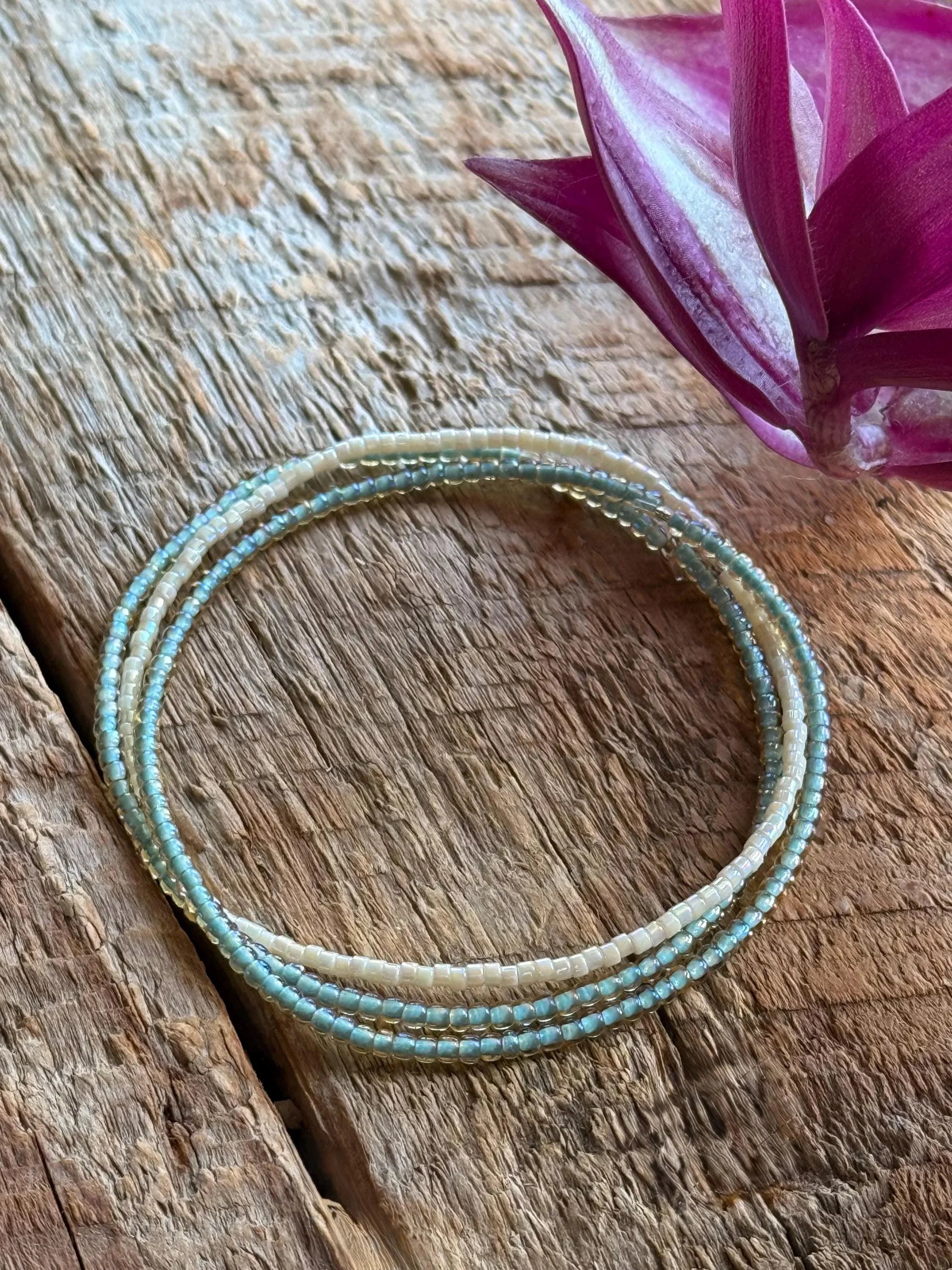 three stretch seed bead bracelets on a wooden surface