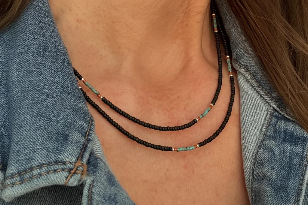 Close-up of a neck wearing handmade glass seed bead necklace with brown and turquoise beads, styled with denim jacket
