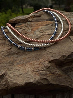 Handmade glass seed bead bracelets in metallic blue, silver, and copper on rock outdoors