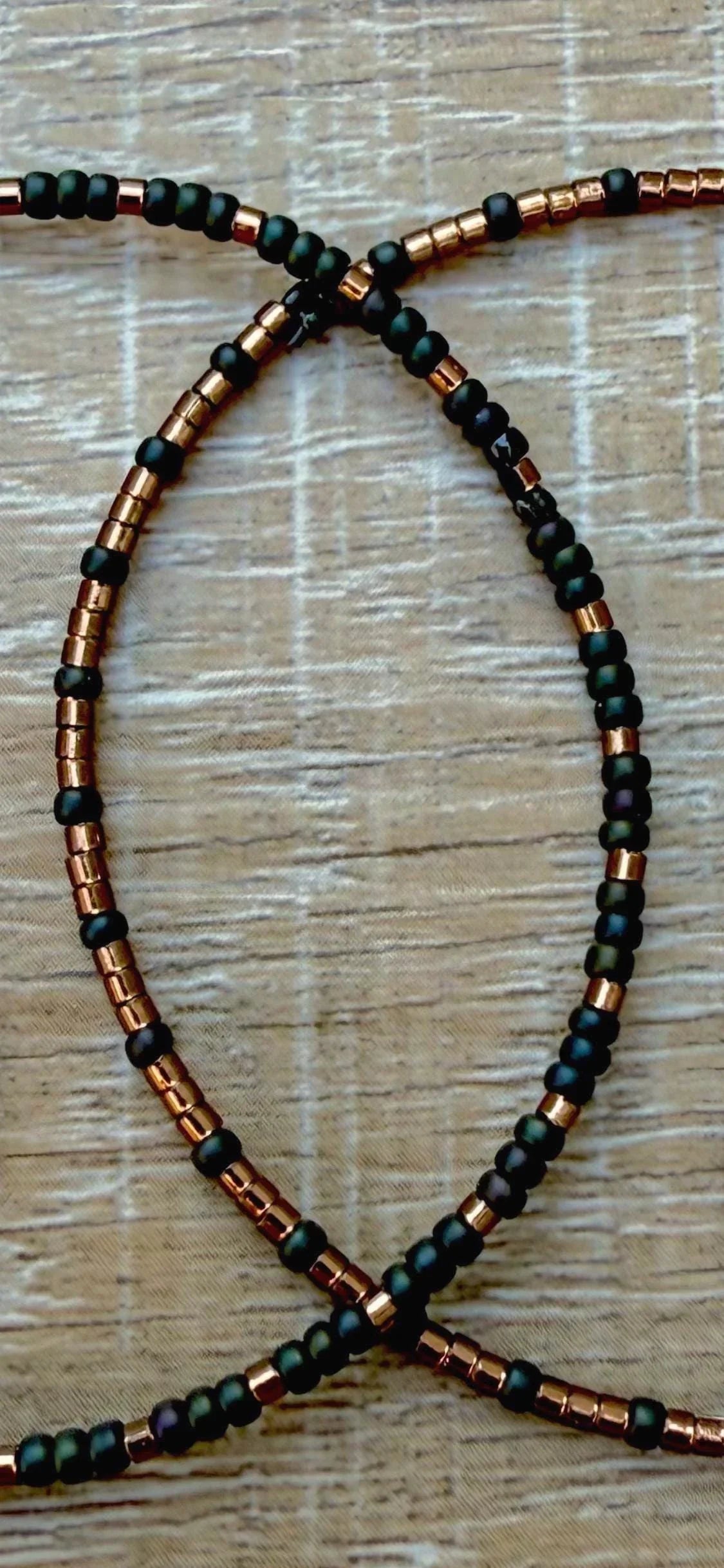 Handmade glass seed bead necklace with matte black and metallic copper beads on wood surface