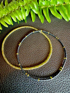 Handmade glass seed bead bracelets in black and gold on textured surface with fern leaf