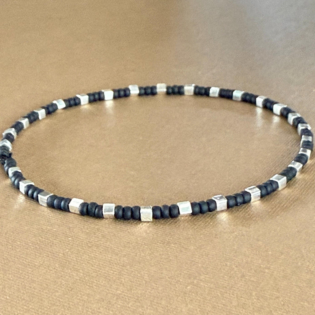 Handmade glass seed bead bracelet with silver cube beads on brown background