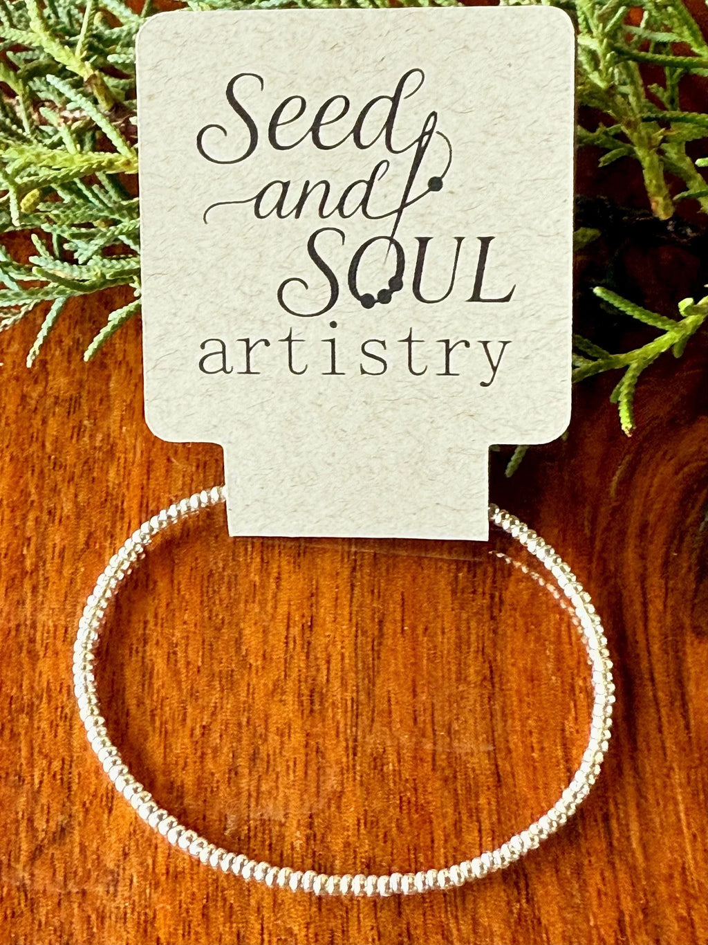 Handmade glass seed bead bracelet on Seed and Soul artistry card, wood background