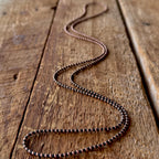Black and copper-plated seed bead necklace laid out on a rustic wooden board.