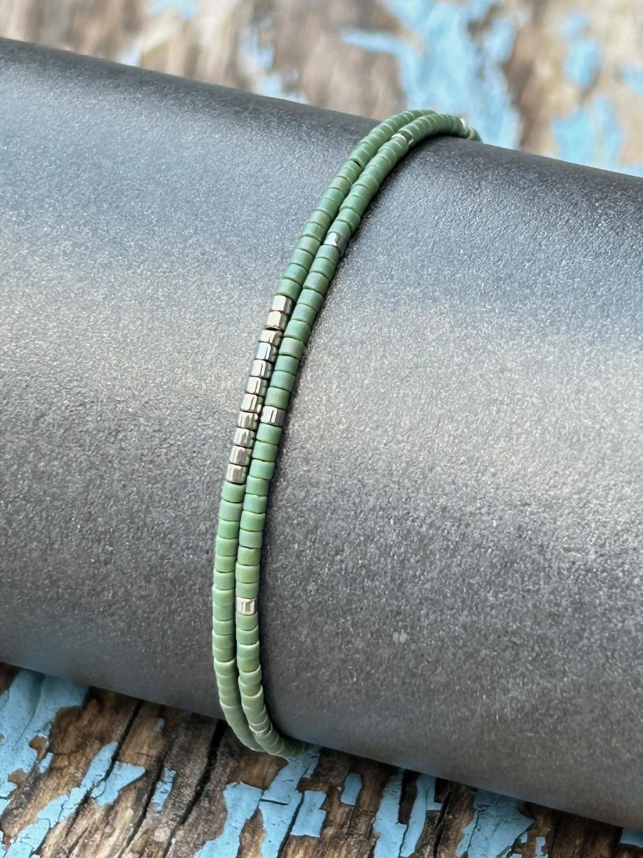 Handmade green glass seed bead bracelet with silver accents on rustic wood background