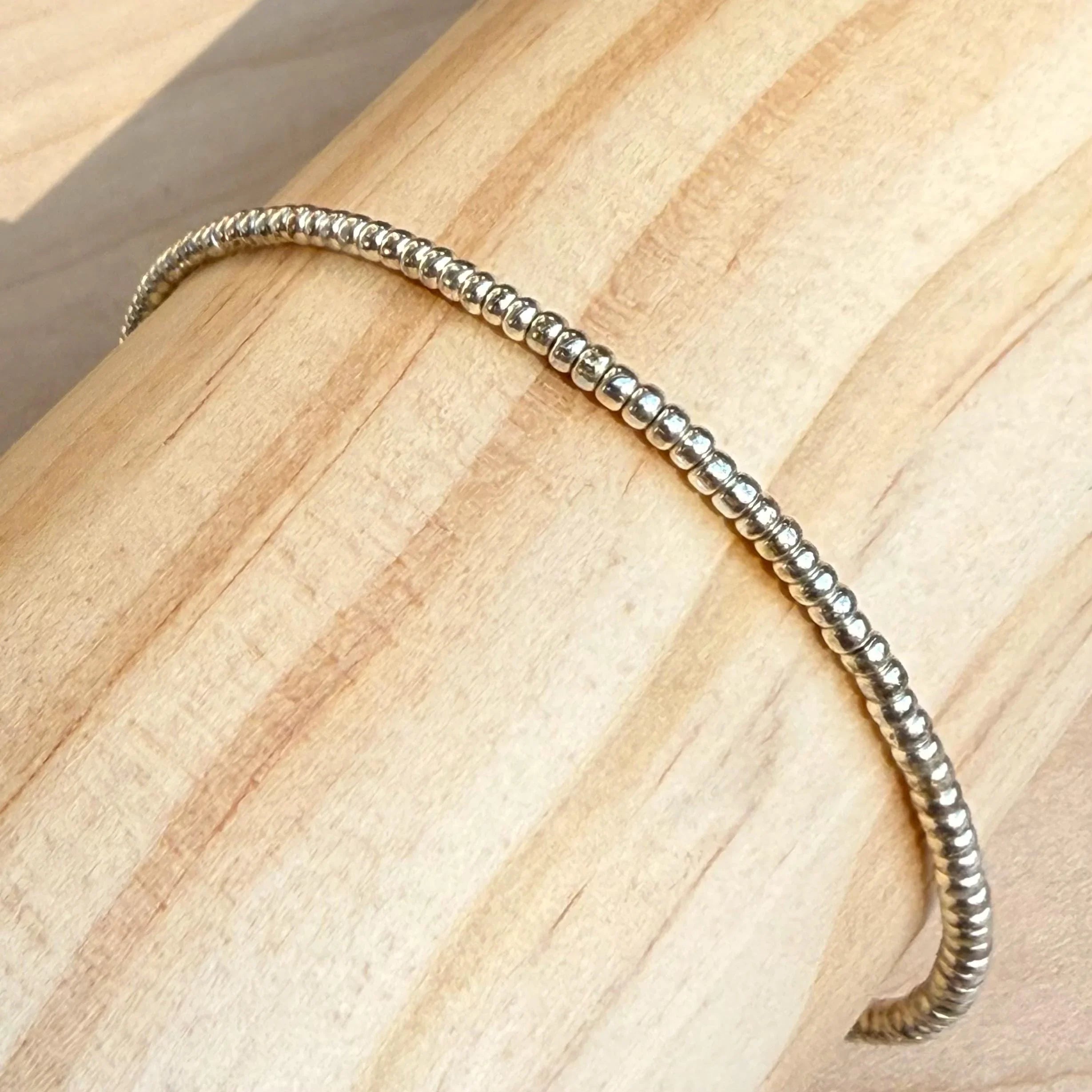 Handmade silver glass seed bead bracelet displayed on light wood by Seed and Soul artistry