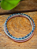 Handmade glass seed bead bracelet with blue, silver, and rose gold beads on wood background