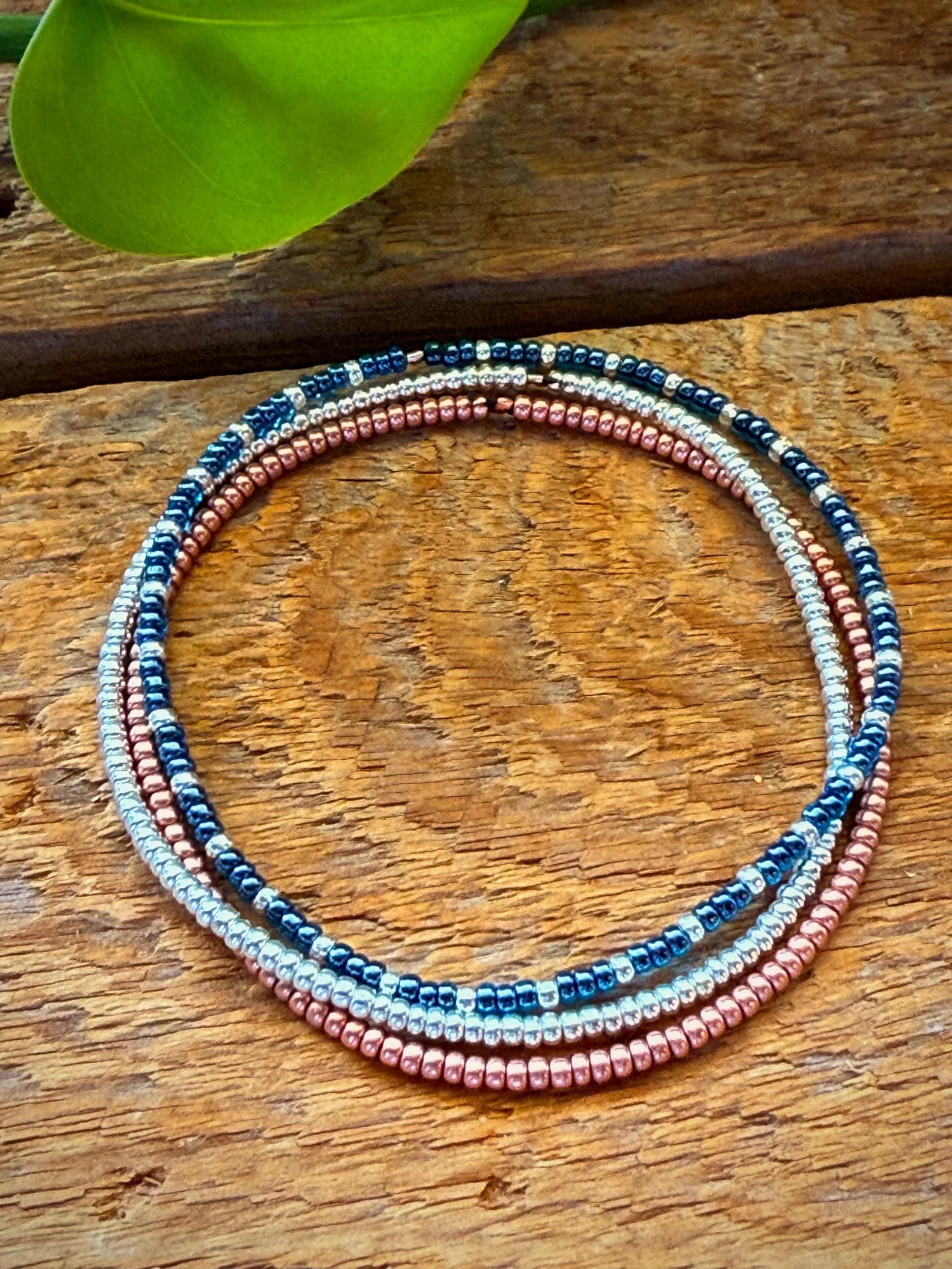 Handmade glass seed bead bracelet with blue, silver, and rose gold beads on wood background
