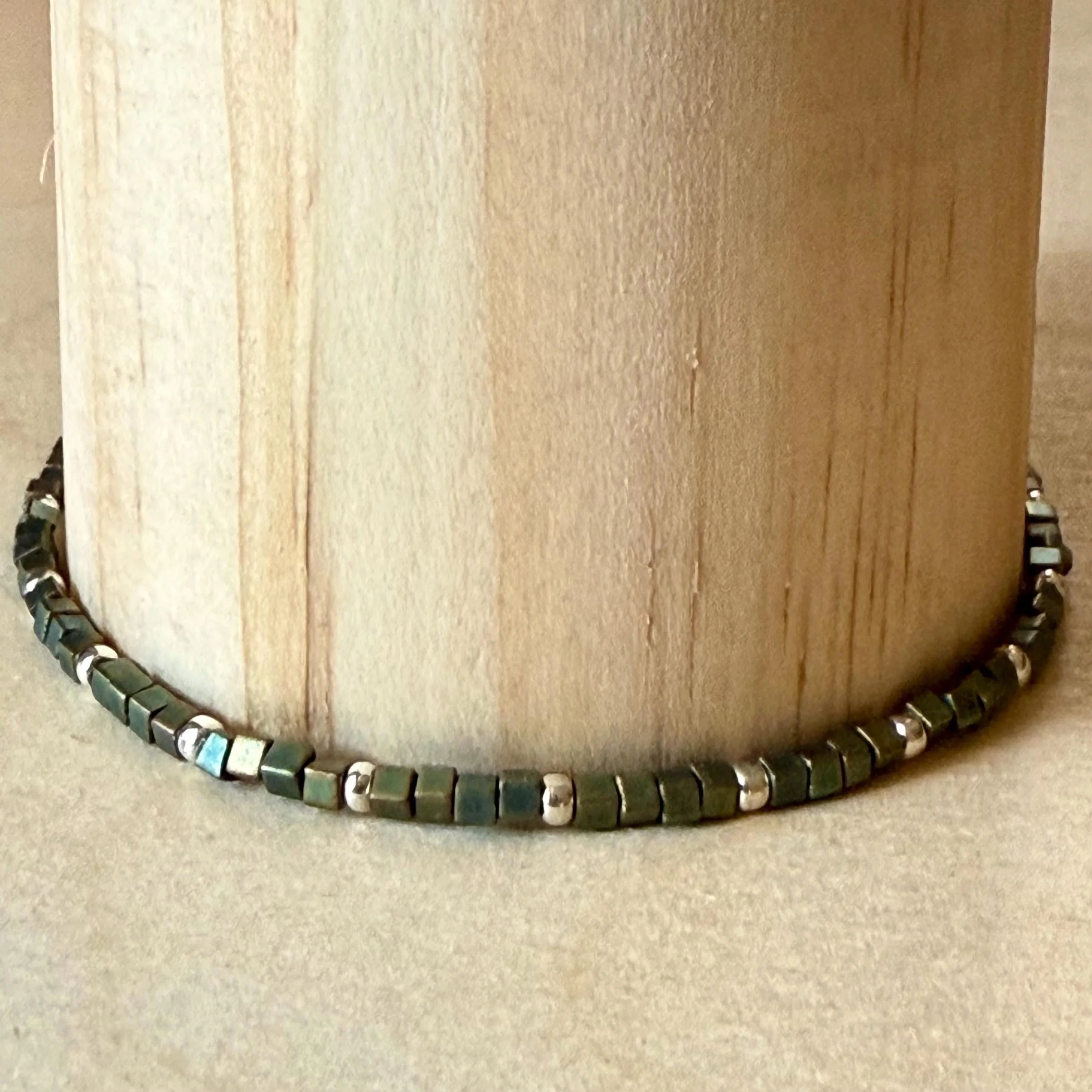 Handmade green and silver glass seed bead bracelet by Seed and Soul artistry on wood display
