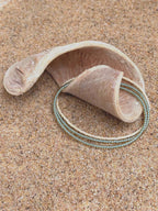 Handmade glass seed bead bracelet with blue and cream beads on sand with driftwood