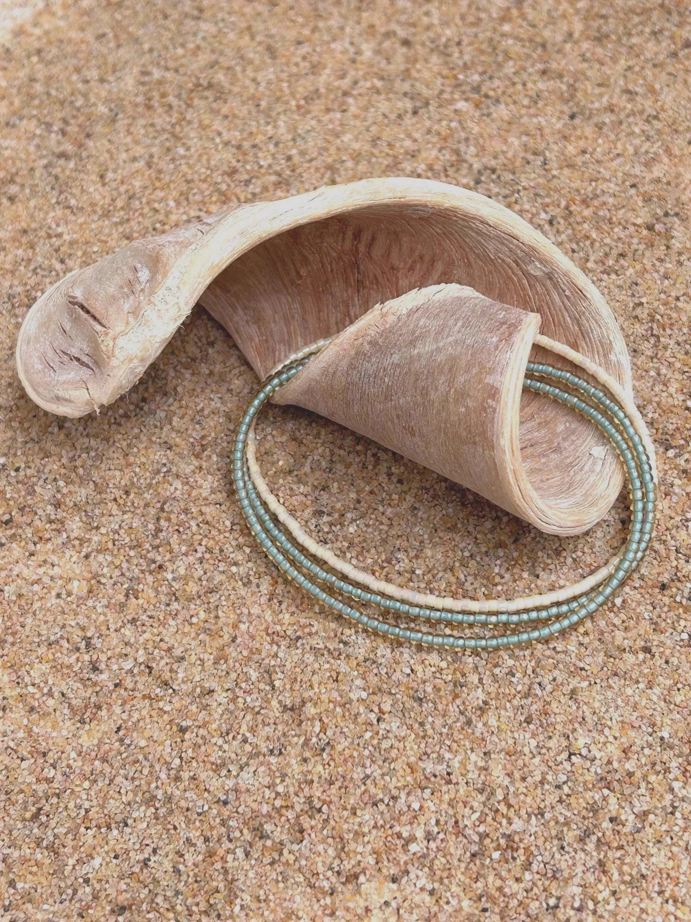 Handmade glass seed bead bracelet with blue and cream beads on sand with driftwood