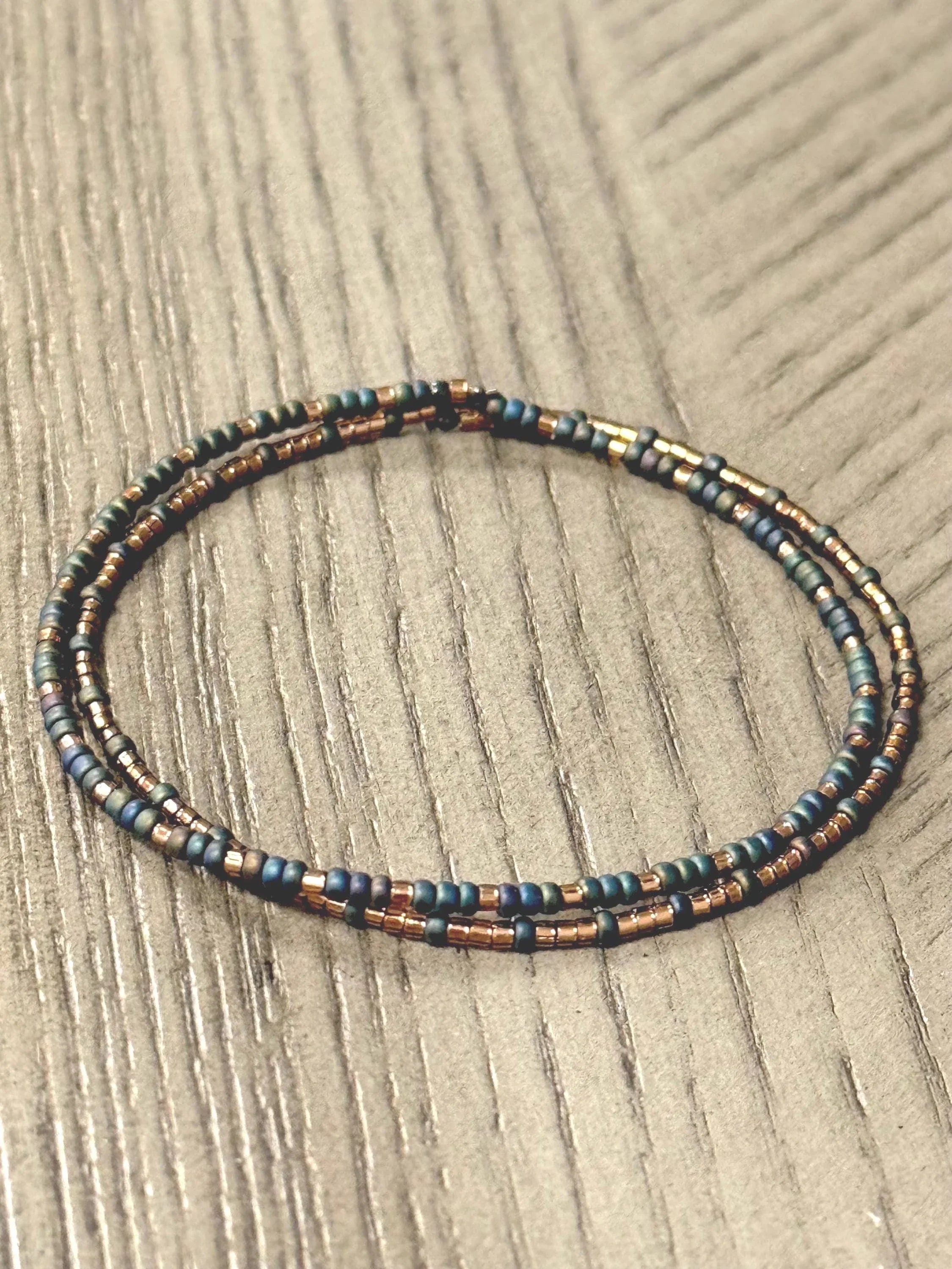 Handmade glass seed bead bracelet with gold and teal beads on wood surface