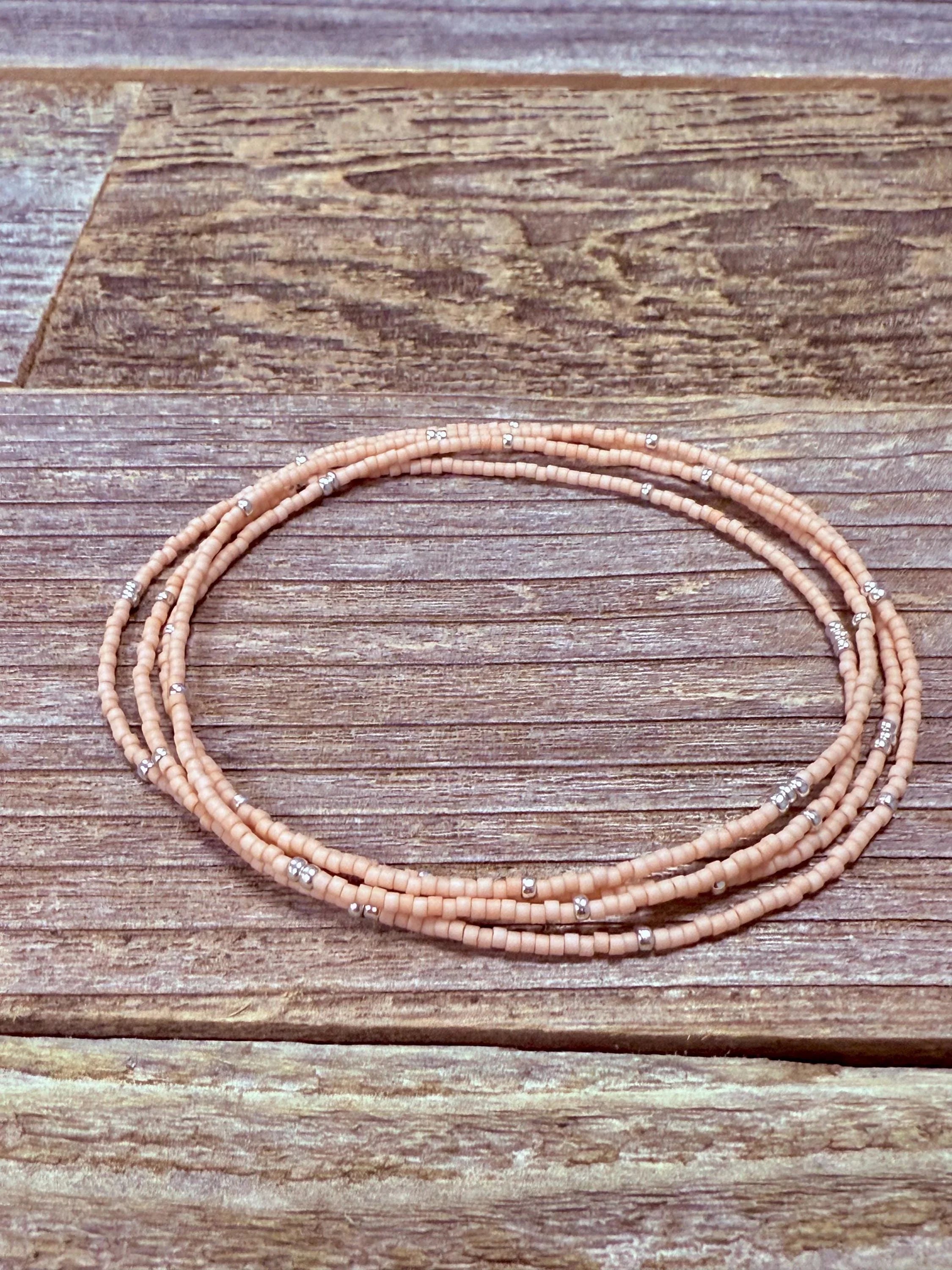 Handmade peach glass seed bead necklace with silver accents on rustic wood background