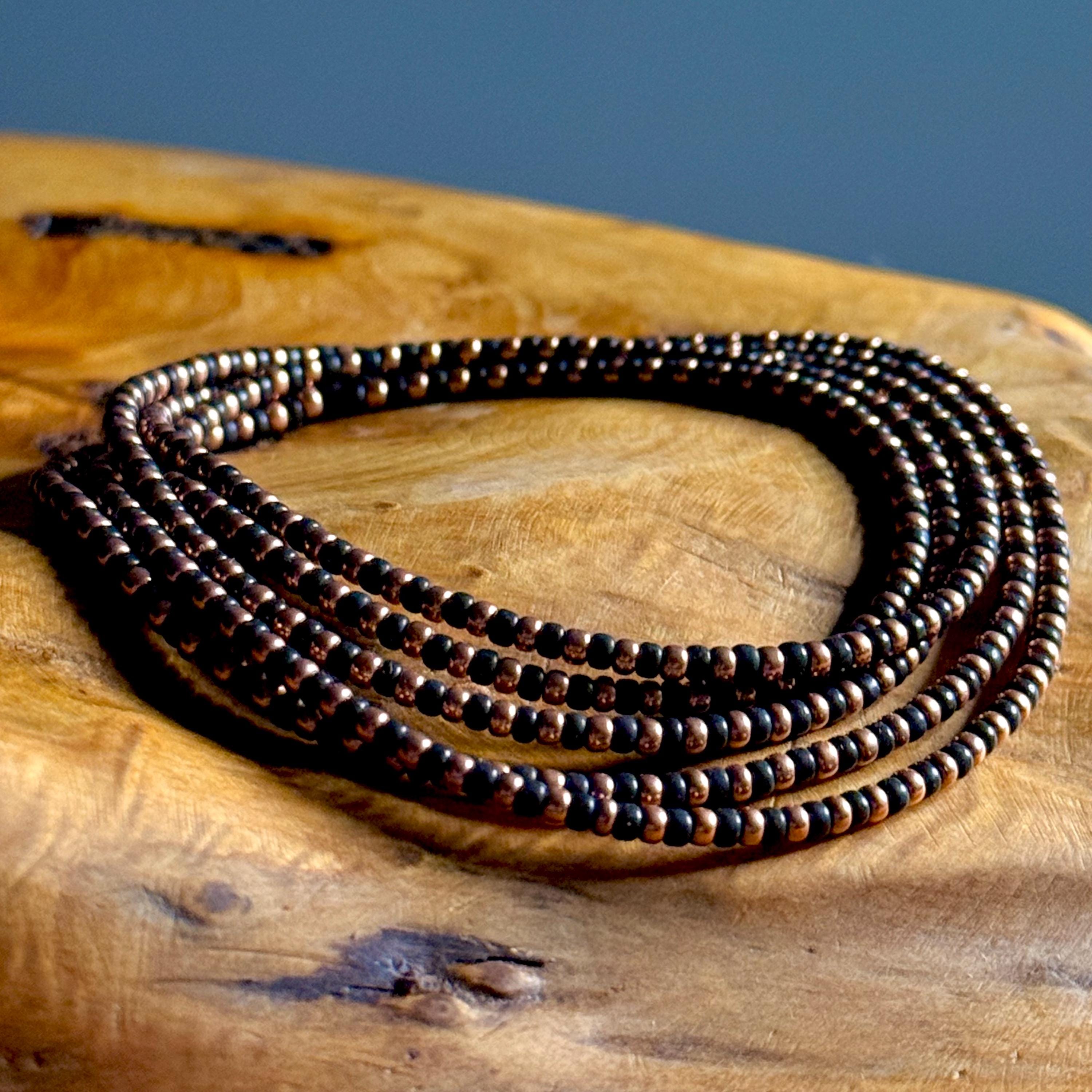 Black and copper-plated seed bead necklace coiled on a wooden background.