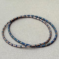 Handmade glass seed bead bracelet in blue and metallic tones on a neutral background