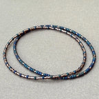Handmade glass seed bead bracelet in blue and metallic tones on a neutral background