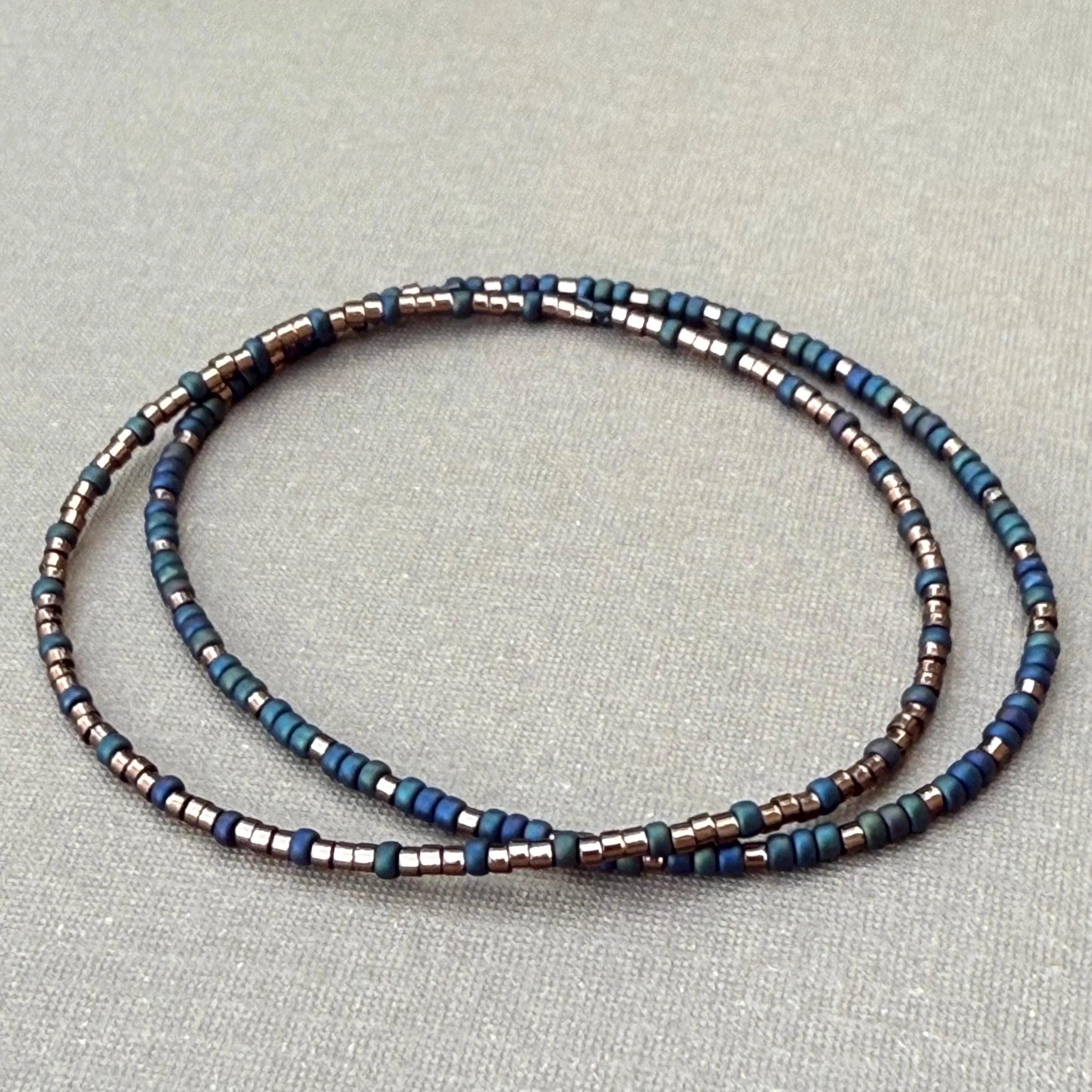 Handmade glass seed bead bracelet in blue and metallic tones on a neutral background