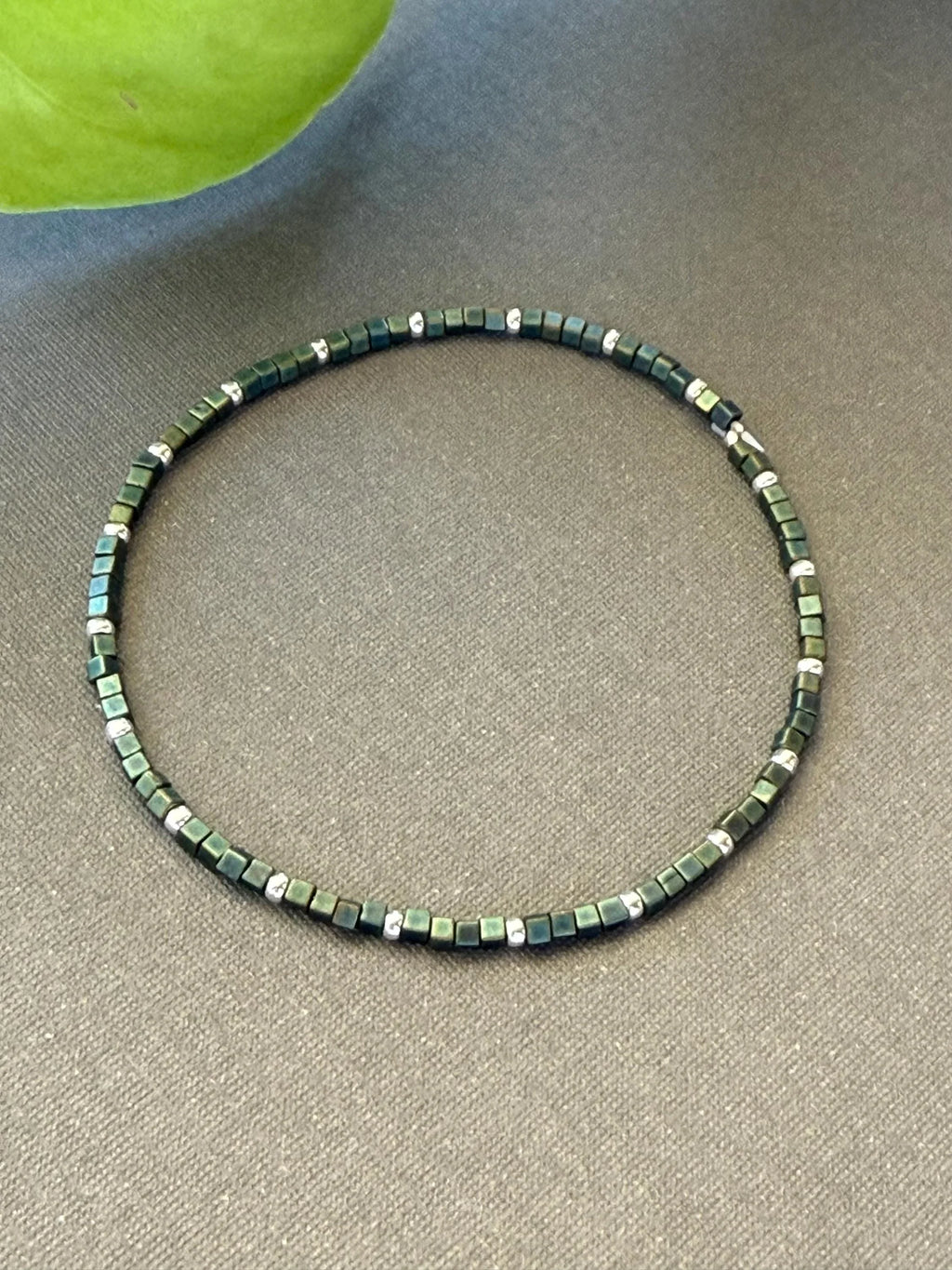 Handmade glass seed bead necklace with green and silver square beads on gray fabric
