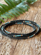 A coiled seed bead wrap bracelet in the colors of brown, turquoise, coral and silver is laid on a wooden board for display.
