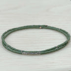 Handmade green glass seed bead bracelet with silver accents on light wood background