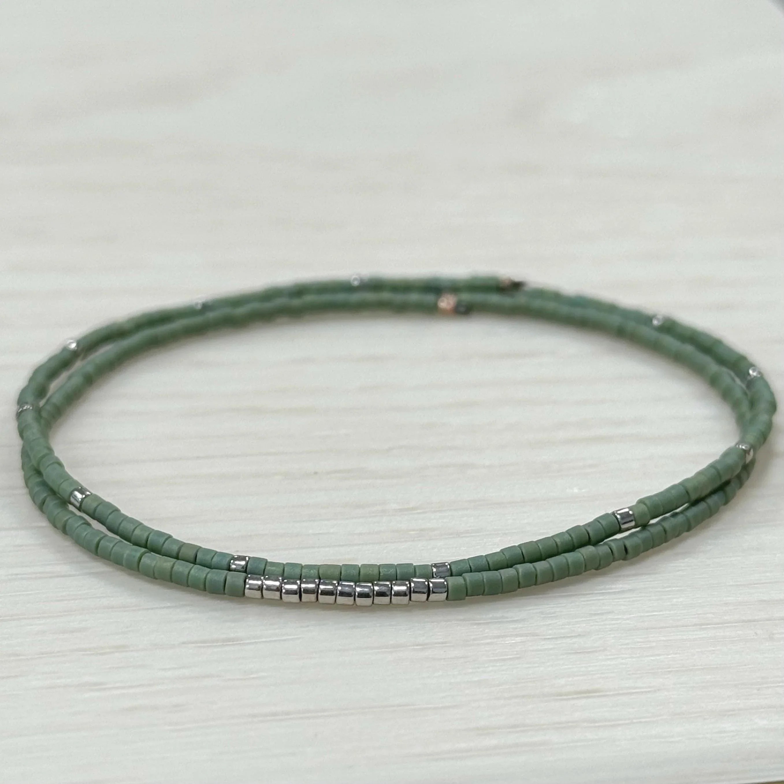 Handmade green glass seed bead bracelet with silver accents on light wood background