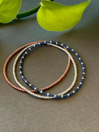 Handmade glass seed bead bracelets in blue, silver, and copper on a neutral background