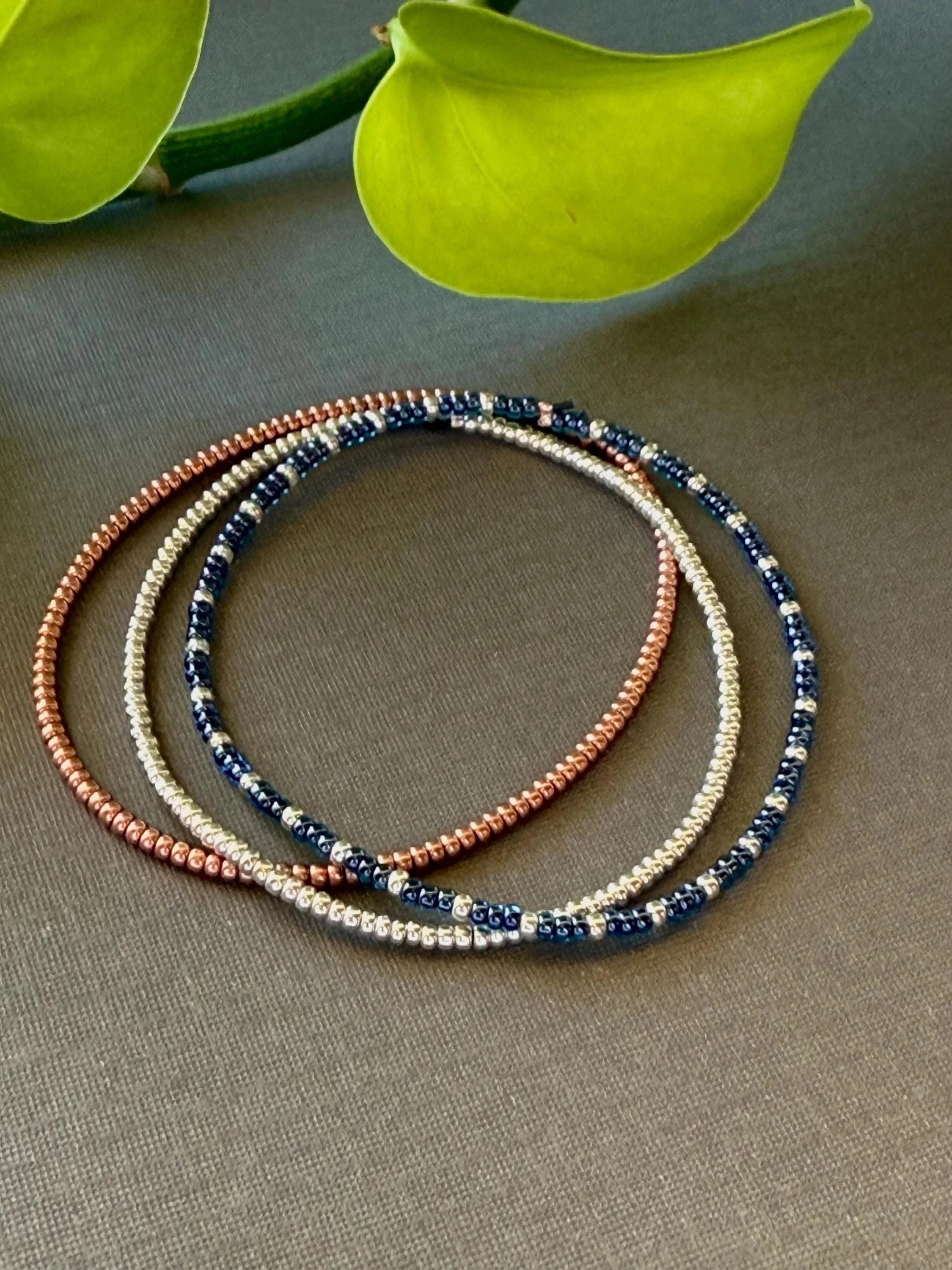 Handmade glass seed bead bracelets in blue, silver, and copper on a neutral background
