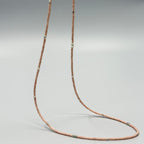 Handmade nude pink glass seed bead necklace with silver accents on a plain background
