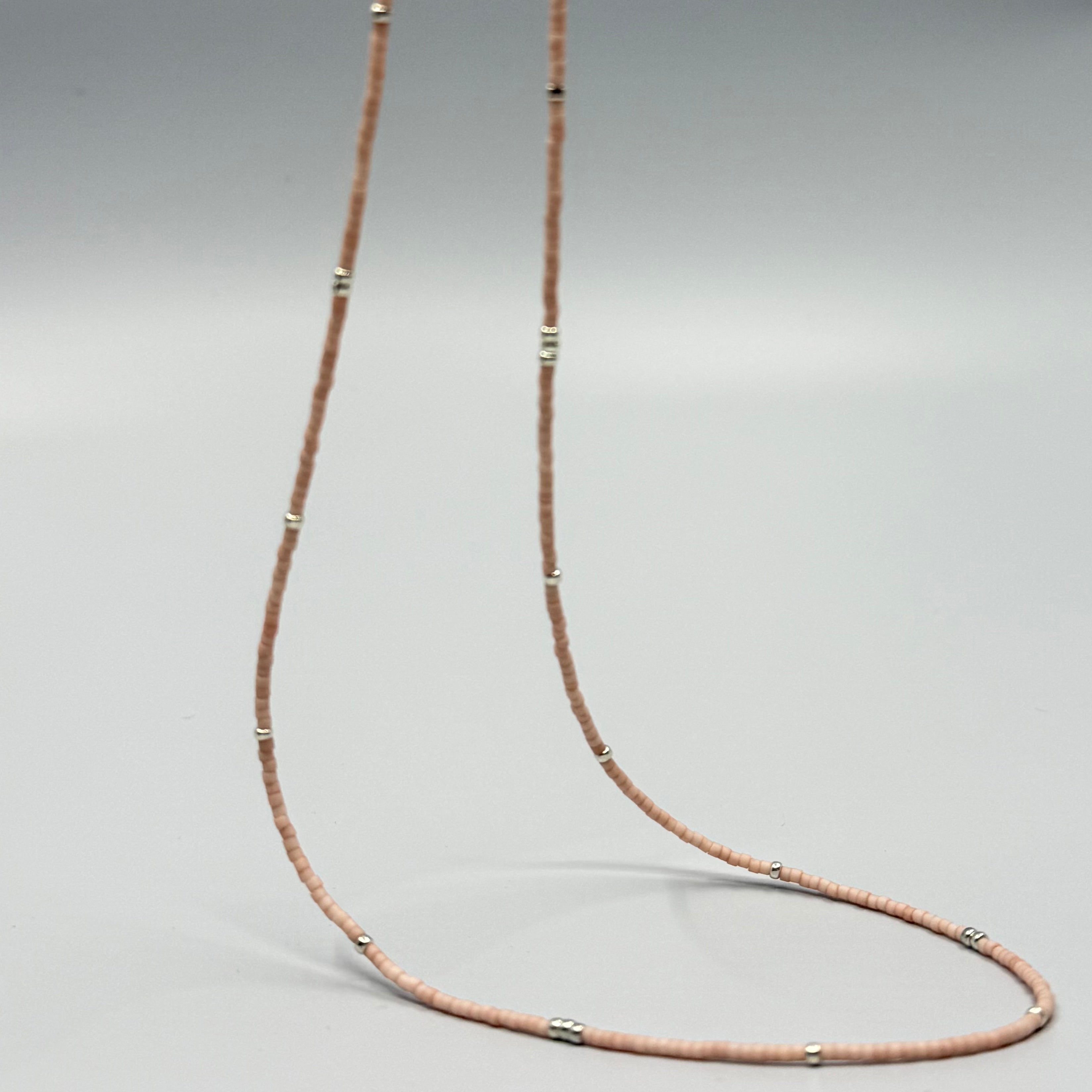 Handmade nude pink glass seed bead necklace with silver accents on a plain background