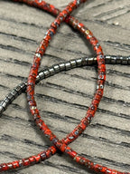 Handmade glass seed bead jewelry strands in red and metallic tones on wood background