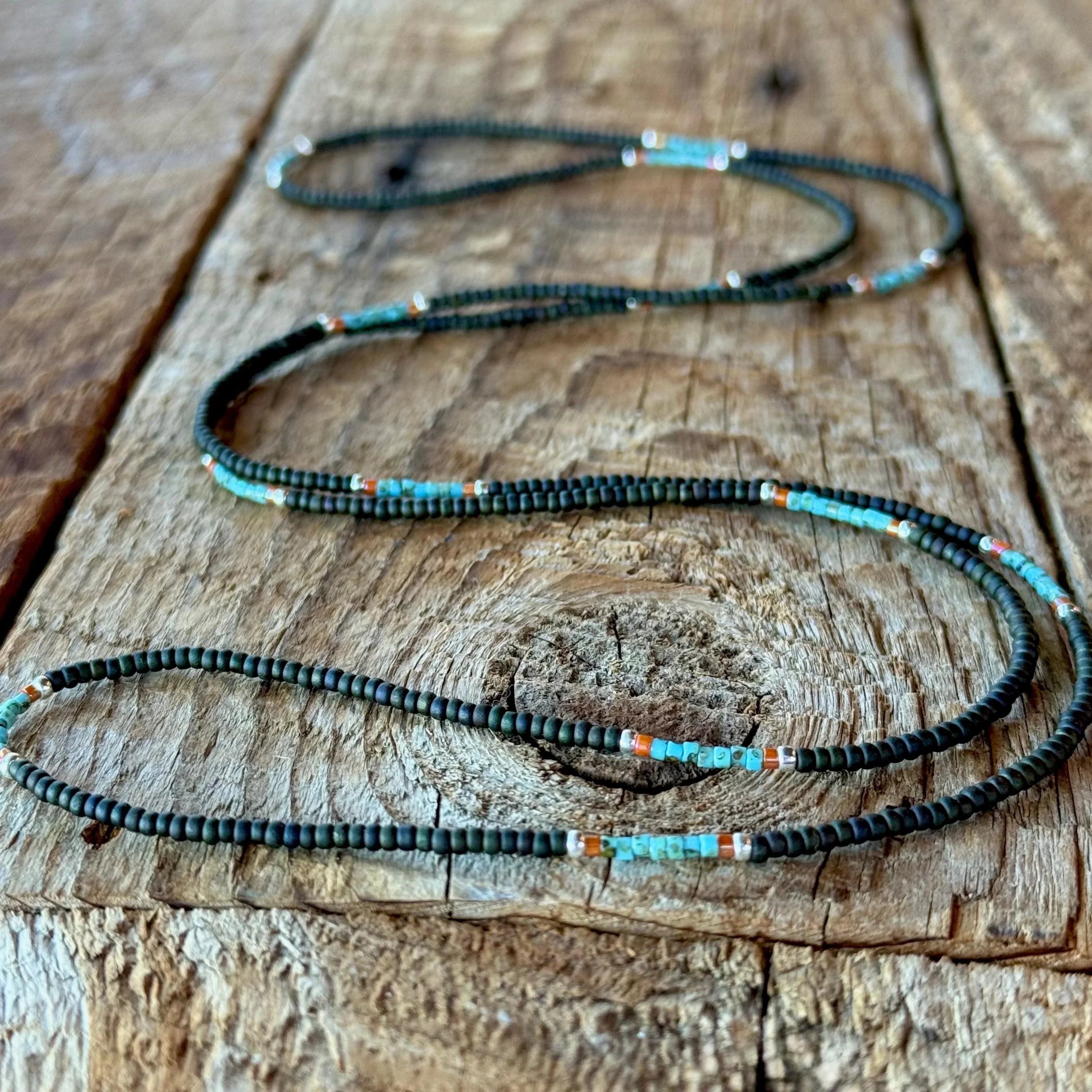 Handmade glass seed bead necklace with brown and turquoise beads laid out on a rustic wooden board.