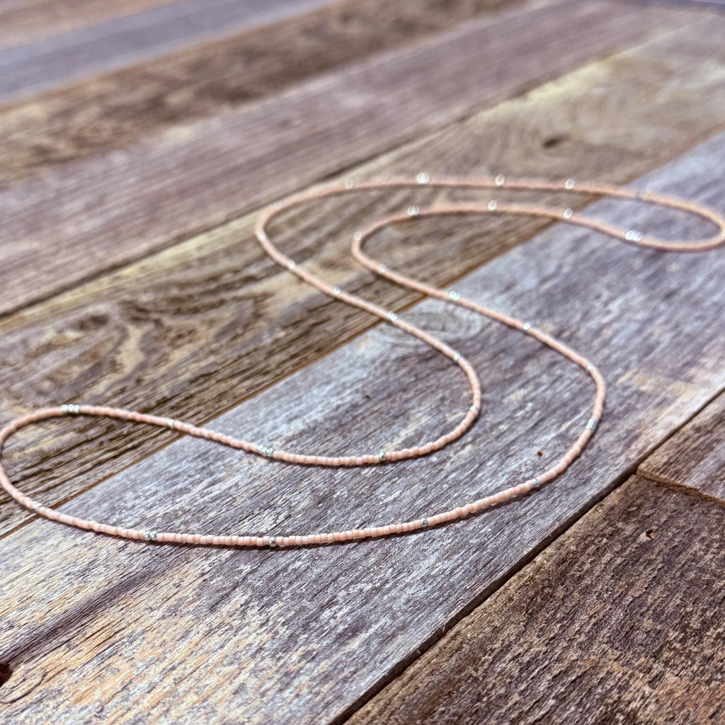 Handmade glass seed bead necklace with pink and silver beads on rustic wood background