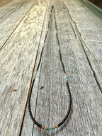 Handmade glass seed bead necklace with green and orange accents on rustic wood, Seed and Soul artistry.