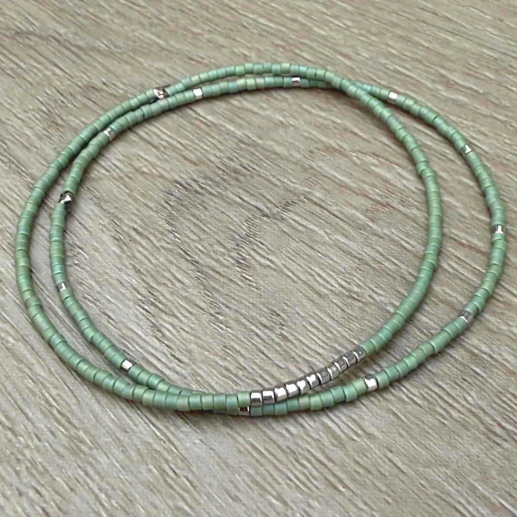 Handmade green glass seed bead bracelet with silver accents on wood surface