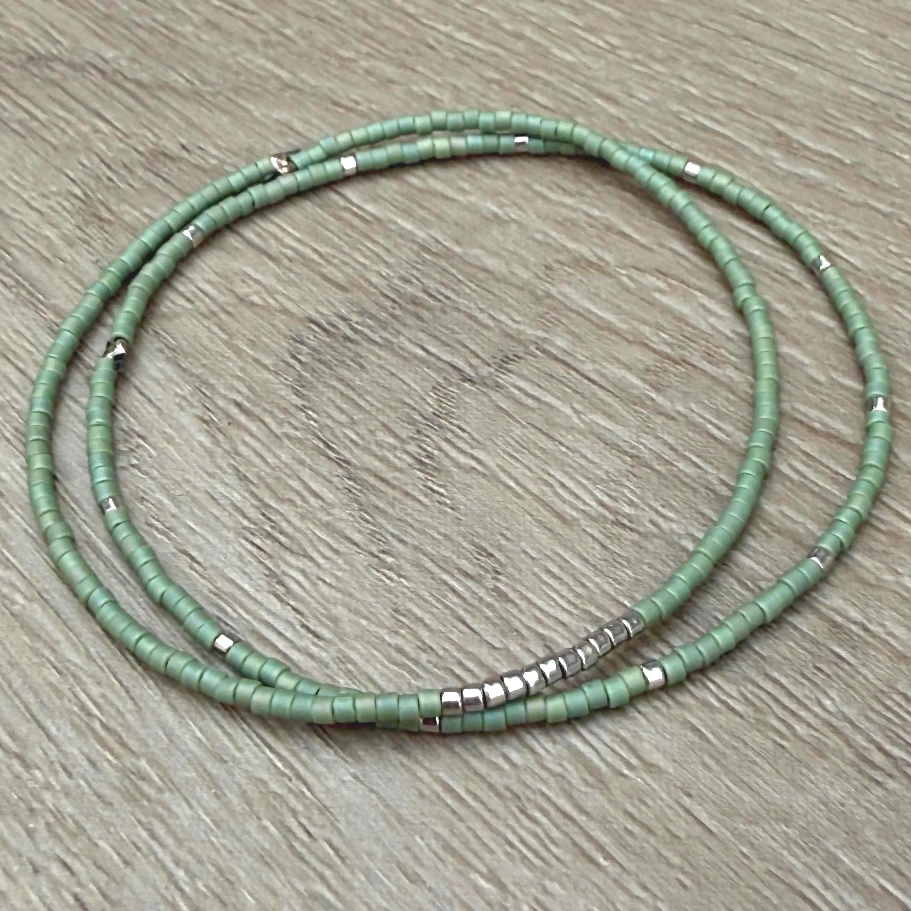 Handmade green glass seed bead bracelet with silver accents on wood surface