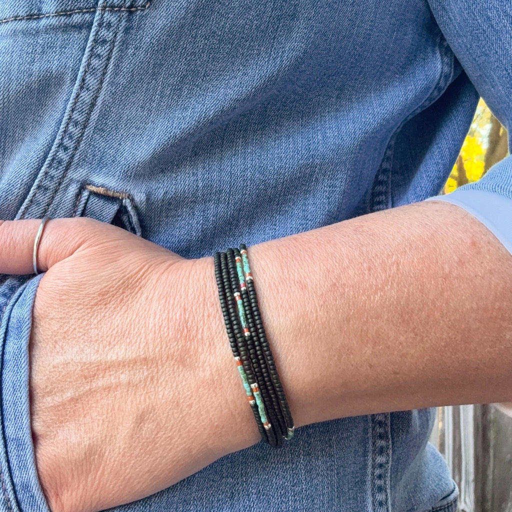 Hand wearing handmade black glass seed bead bracelet, blue denim jacket background.