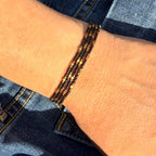 Four handmade glass seed bead bracelets in black and gold shown on wrist, Seed and Soul artistry