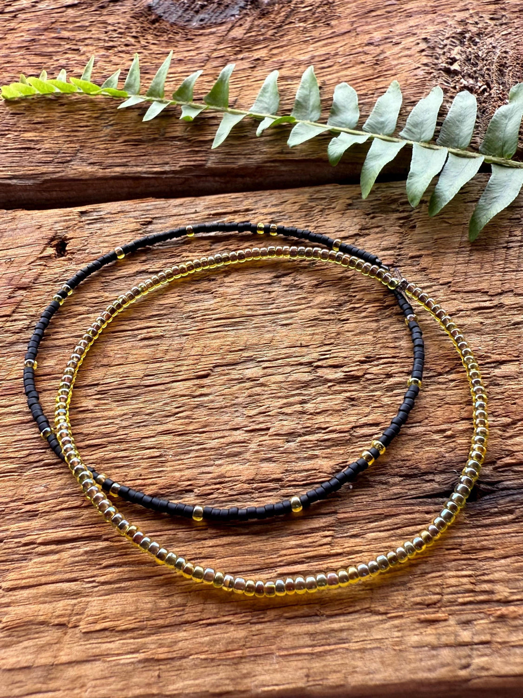 Handmade black and yellow glass seed bead bracelets on rustic wood with fern, Seed and Soul artistry