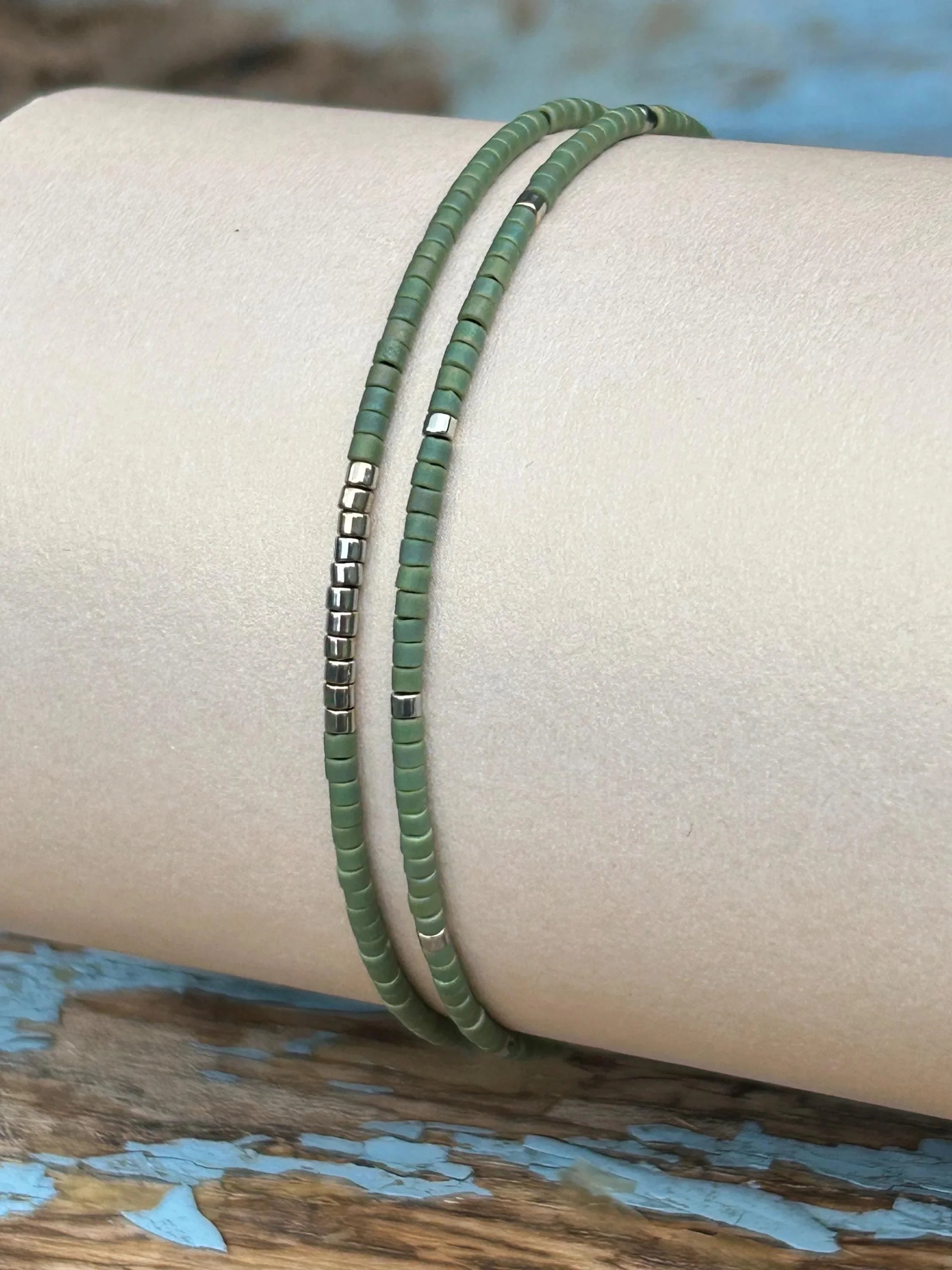 Handmade green glass seed bead bracelet with metallic accents on neutral display