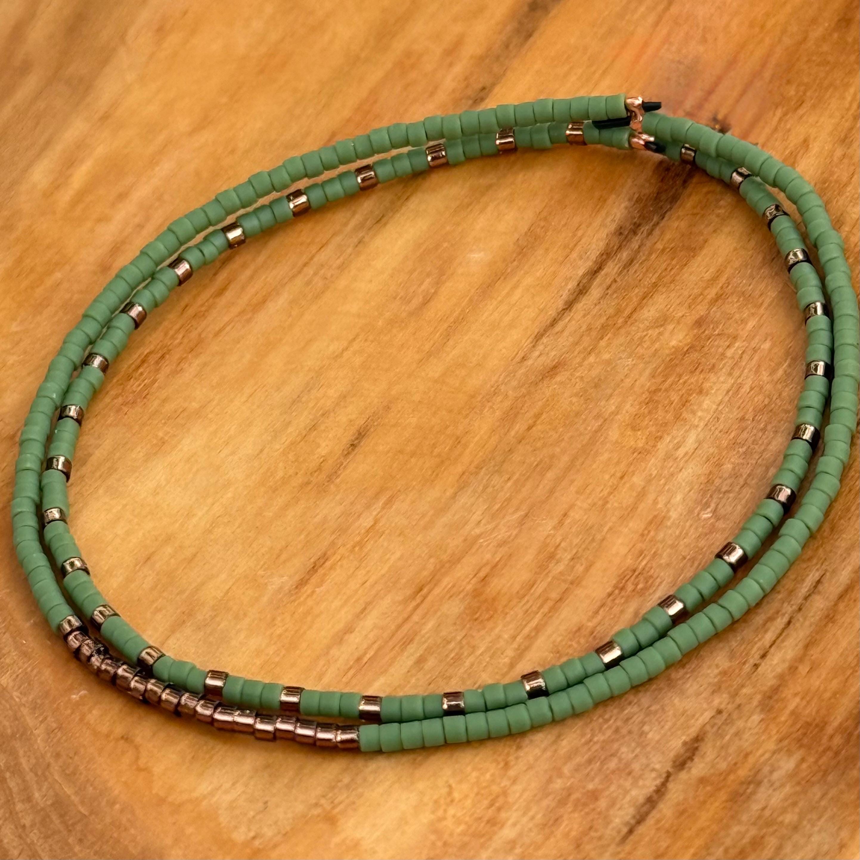 Handmade green and bronze glass seed bead bracelet set on wood surface