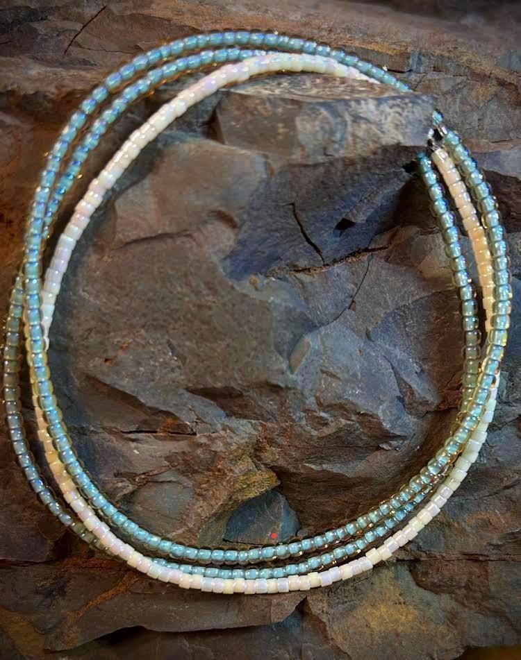 Handmade glass seed bead necklace with blue and white beads on a stone background